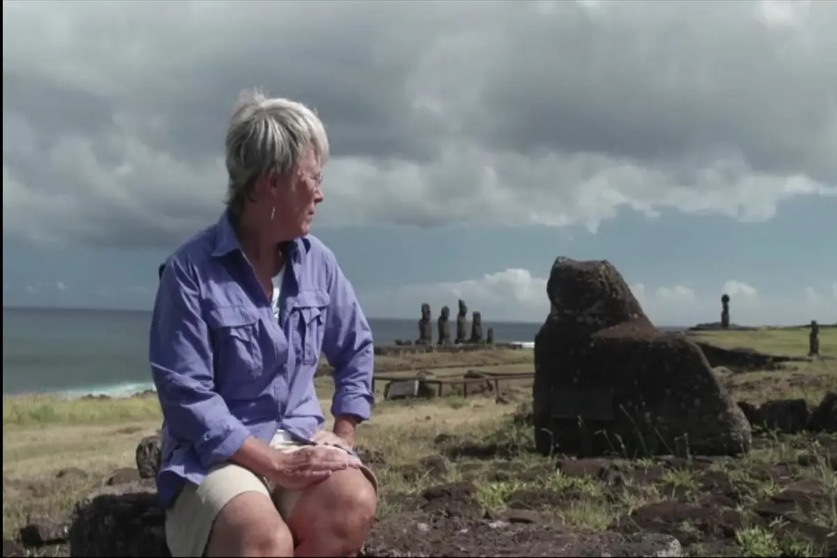 Una mujer sentada en la Isla de Pascua con estatuas Moai al fondo.