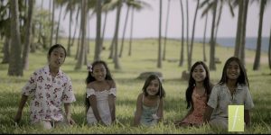 Niñas y niños sonrientes sentadas en el césped en un paisaje de palmeras en la Isla de Pascua.