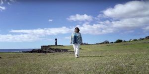 Mujer caminando en la Isla de Pascua con una estatua Moái al fondo.