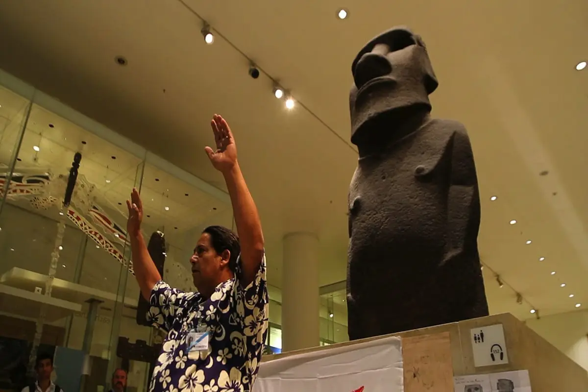 Hombre levantando los brazos junto a un moái en un museo.