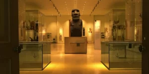 Moái Hoa Hakananai'a en una galería de museo, rodeado de vitrinas con artefactos culturales.